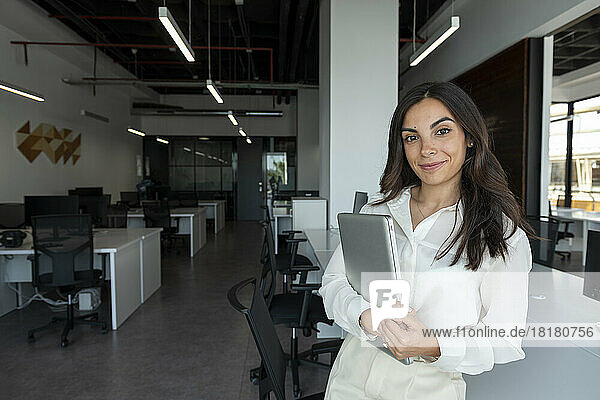 Smiling young businesswoman with laptop at desk in office
