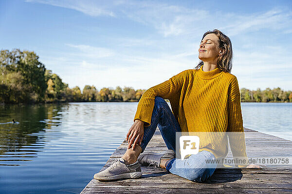 Smiling woman sitting on jetty under sky