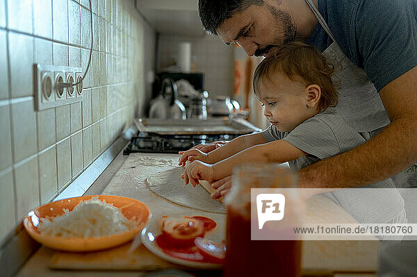 Father and son rolling pizza dough together in kitchen at home