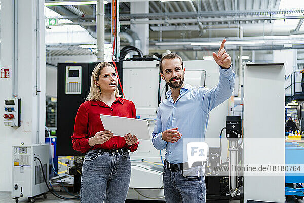 Businessman gesturing by colleague holding tablet PC at factory