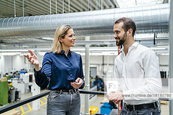 Smiling businesswoman gesturing and talking to colleague near railing at factory
