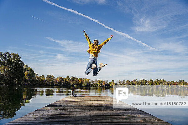 Carefree woman jumping on jetty under vapor trail