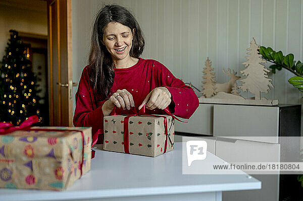 Glückliche Frau  die zu Hause eine Schleife an Weihnachtsgeschenken bindet
