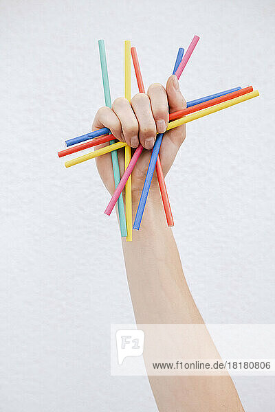Hand of woman holding colored pencils in front of white wall