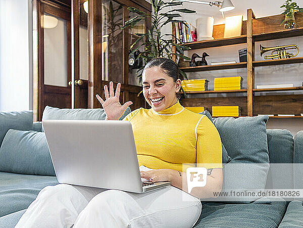 Happy businesswoman waving on video call through laptop on sofa