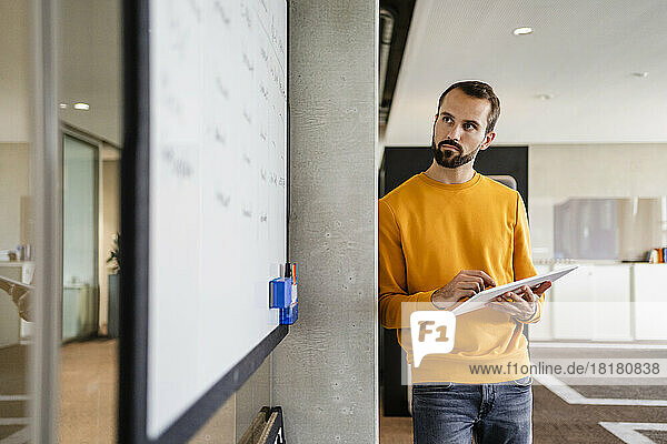Entschlossener Geschäftsmann mit Tablet-PC blickt auf Whiteboard im Büro
