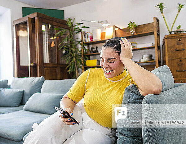 Happy young woman holding mobile phone on sofa