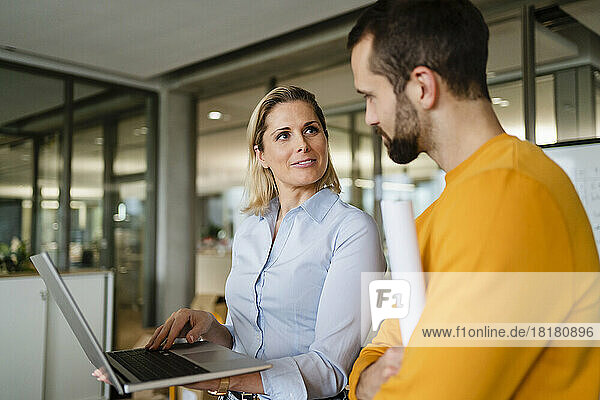 Smiling businesswoman with laptop looking at colleague in office