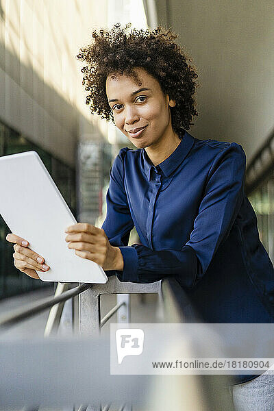 Smiling businesswoman holding tablet PC leaning on railing