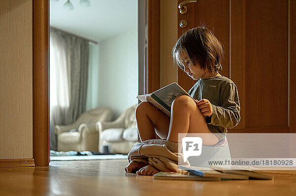 Netter Junge sitzt auf dem Töpfchen und liest zu Hause ein Buch