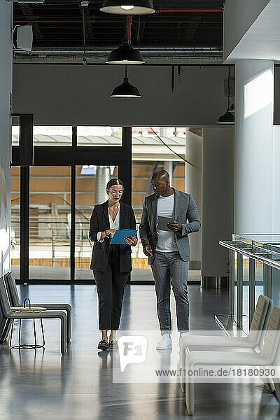 Business colleagues walking and discussing over clipboard in office corridor