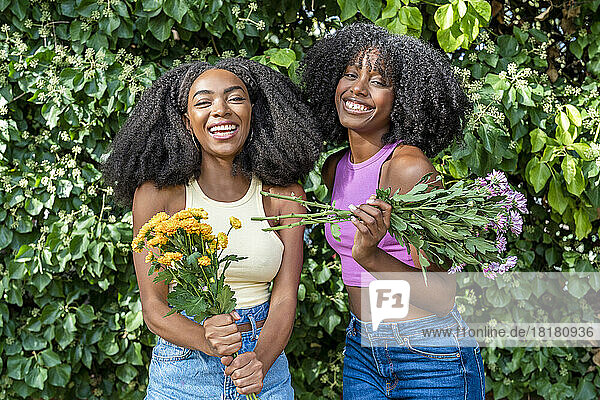 Happy friends holding flowers in front of plant