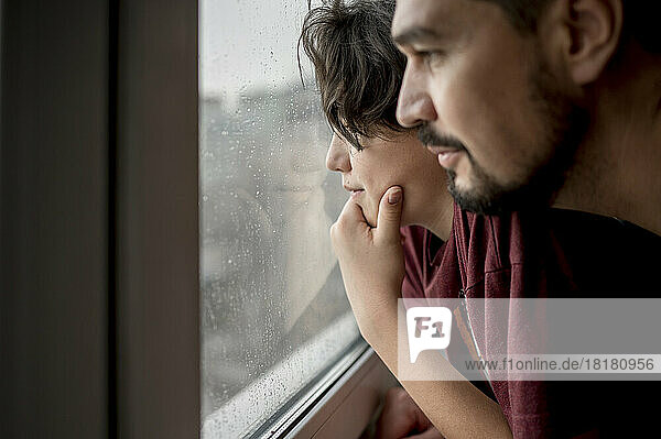 Vater und Sohn schauen zu Hause durch das Fenster