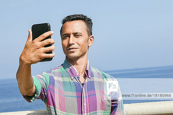 Lächelnder Mann macht ein Selfie mit dem Smartphone vor dem Meer