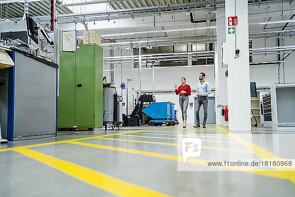 Businesswoman walking with colleague on markings in production hall at factory