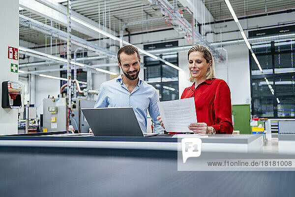 Businesswoman reviewing document by colleague using laptop at factory