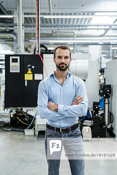 Confident businessman standing with arms crossed at factory
