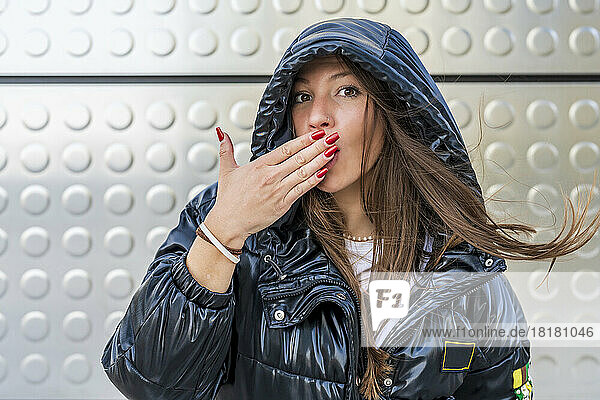 Woman covering mouth with hand in front of metal wall
