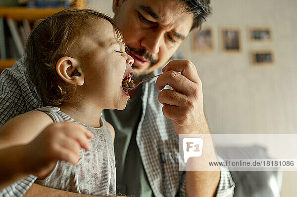 Father feeding porridge with spoon to son at home