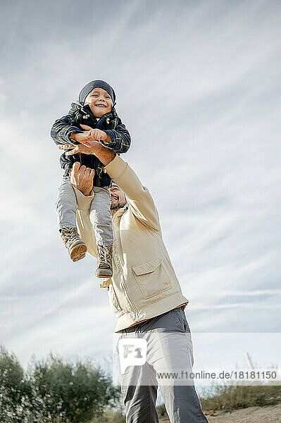 Happy boy enjoying with father in front of sky at beach