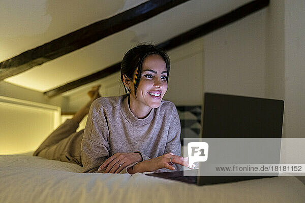 Smiling young woman using laptop on bed in bedroom