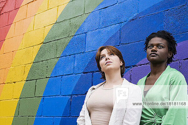 Thoughtful young woman with friend in front of rainbow colored wall