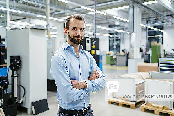Smiling businessman with arms crossed at factory