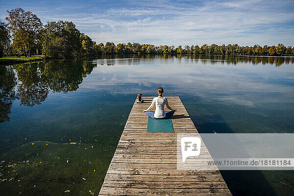 Frau meditiert vor einem See unter freiem Himmel