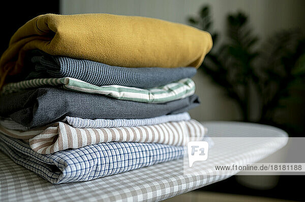 Stack of folded clothes on ironing board at home