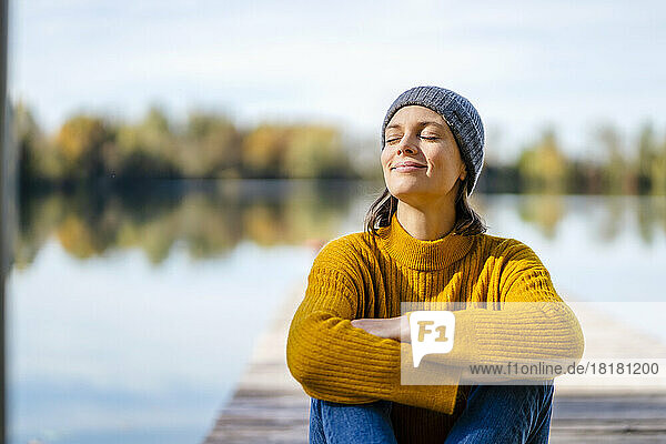 Smiling woman with arms crossed and eyes closed sitting on jetty