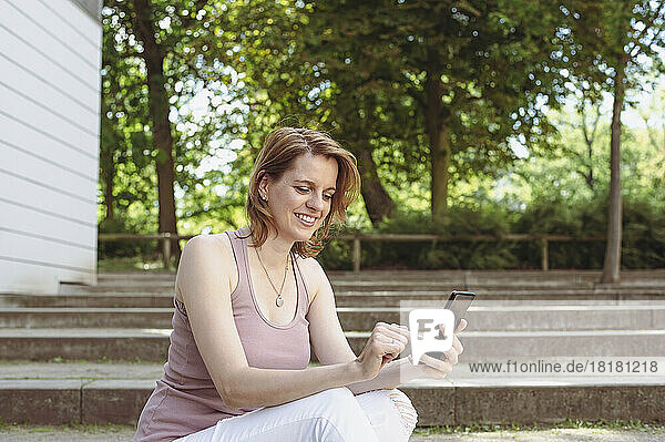 Glückliche Frau  die im Park Textnachrichten auf dem Smartphone sendet
