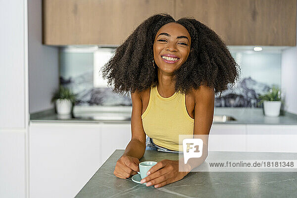 Happy Afro woman with coffee cup in kitchen