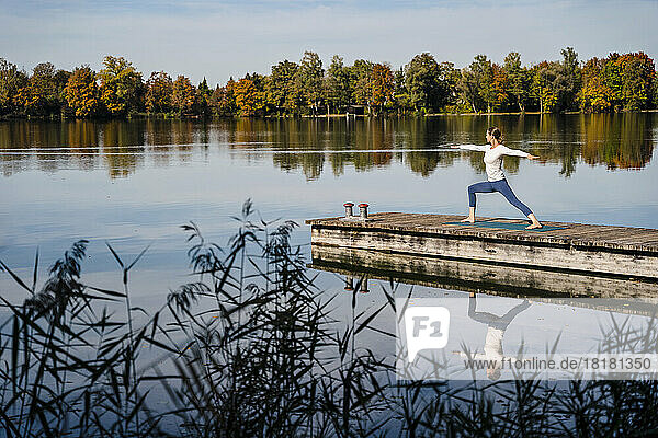 Woman with arms outstretched practicing yoga on jetty