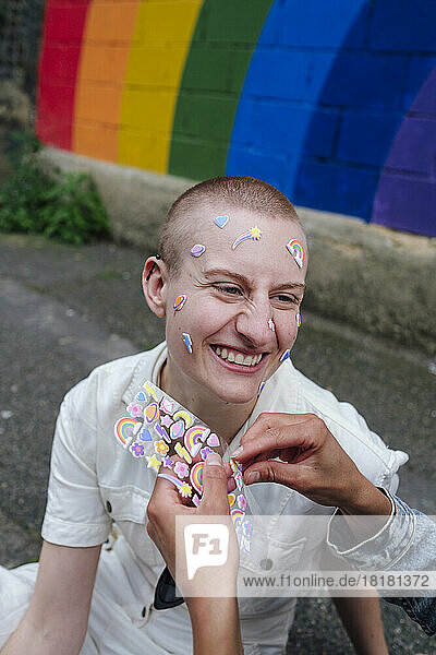 Woman sticking sticker on face of happy non-binary person