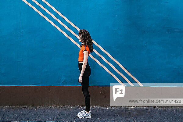 Young woman standing on footpath in front of blue wall