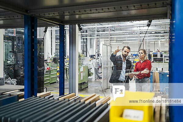 Colleague gesturing by businesswoman standing in production hall