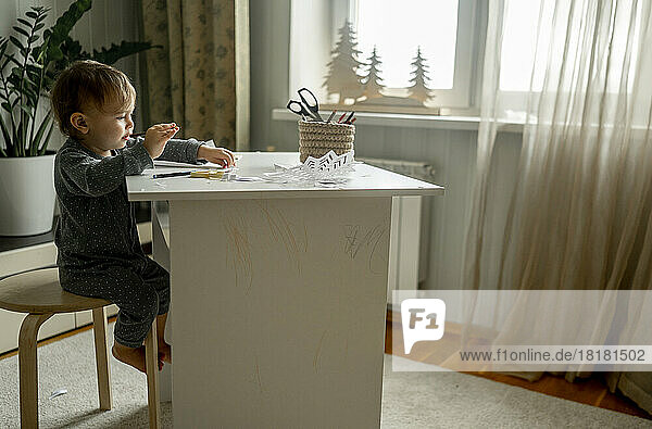 Kleiner Junge sitzt zu Hause auf einem Hocker neben dem Tisch