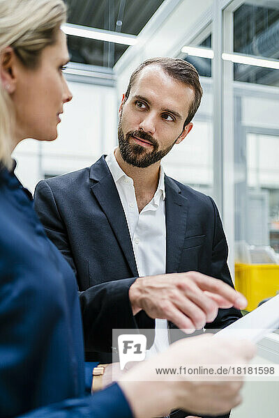 Businessman pointing and looking at colleague with document in factory