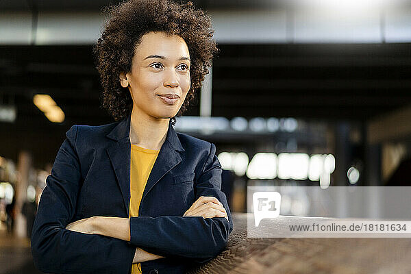 Smiling businesswoman with arms crossed day dreaming by railing