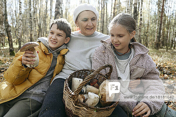 Ältere Frau schaut Mädchen an  das neben einem Jungen sitzt und Pilze im Wald hält