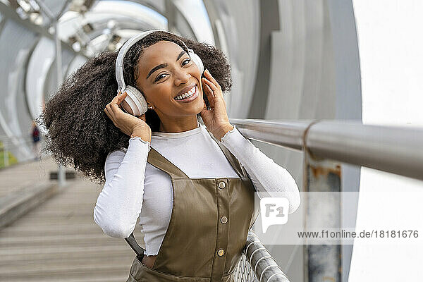 Happy young woman enjoying listening to music on bridge