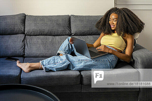 Relaxed Afro woman using laptop in living room at home