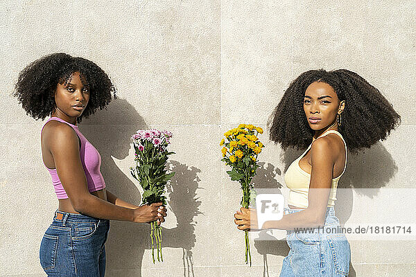 Woman with friend holding flowers in front of white wall