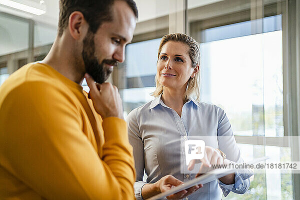 Smiling businesswoman explaining colleague through tablet PC at office