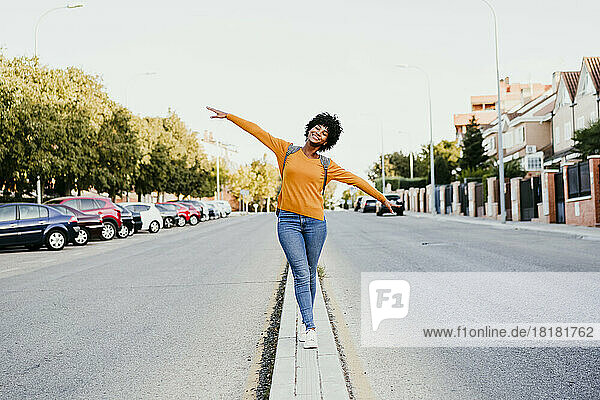 Happy young woman walking with arms outstretched on road