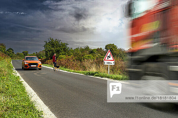 Man crossing road with dog by moving vehicles on road