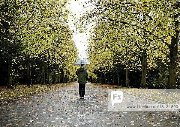 Senior woman with umbrella walking on road amidst autumn trees