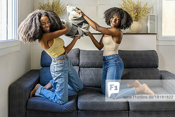 Cheerful multiracial lesbian couple doing pillow fight on sofa