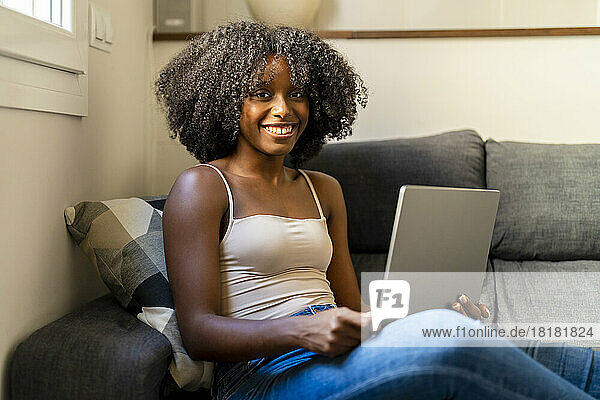 Happy woman with laptop sitting on sofa in living room
