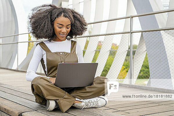 Young woman using laptop sitting cross-legged on footbridge